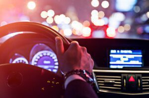 An image of the driver’s view of the road at night, with the dashboard of the car lit up.